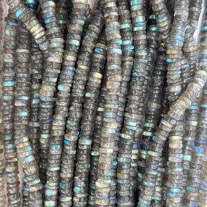 May include: A strand of gray and iridescent labradorite gemstone beads. The beads are small and round, and they have a smooth, polished finish.