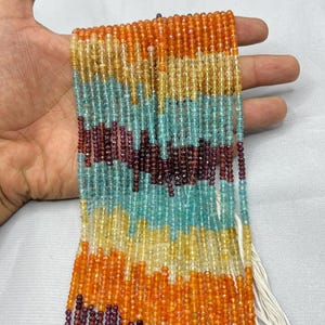 Può includere: Fili di perline colorate di pietre preziose nei toni dell'arancione, giallo, verde acqua e bordeaux. Le piccole perline sfaccettate sono infilate con filo bianco. Le perline sono tenute in mano su sfondo bianco.