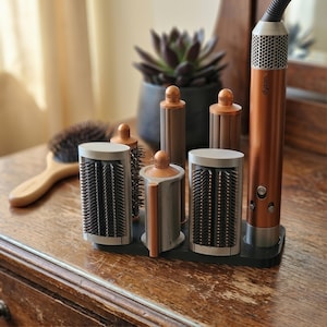 May include: A copper and silver hair styling tool set with multiple attachments, including brushes and rollers, displayed on a wooden surface. A wooden hairbrush and a potted succulent are also visible in the background.