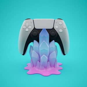 May include: A white and black video game controller rests on a stylized crystal formation. The crystal is a gradient of blue and purple, sitting on a pink base. The background is a solid teal color.