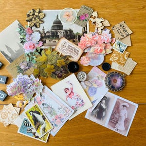 May include: A collection of vintage-style paper ephemera including postcards featuring St. Paul's Cathedral, floral cutouts, black and white photographs of people, small animal illustrations, postage stamps, black buttons, and wooden letter blocks.