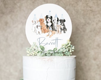 May include: A white two-tier cake with green foliage and a round cake topper featuring a group of dogs wearing party hats. The topper says "Barrett".