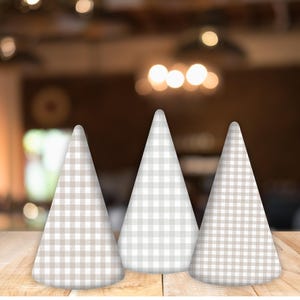 May include: Three white and brown gingham party hats in the shape of cones. The hats are sitting on a wooden surface.