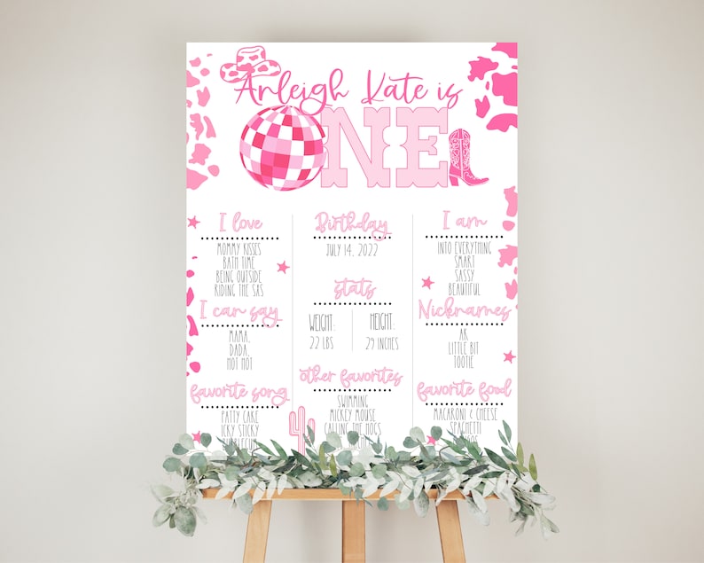 May include: A pink and white printable birthday sign for a one-year-old girl. The sign features a disco ball, cowboy boots, and a pink and white cow print pattern. The sign includes the girl's name, Arleigh Kate, and her birthday, July 14, 2022. It also lists her favorite things, including mommy kisses, bath time, and her favorite songs.