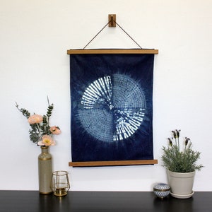 Peut inclure: Une tenture murale en tissu indigo teinté de bleu et de blanc avec un motif circulaire. Le tissu est tendu sur un cadre en bois et suspendu à un mur avec un crochet en bois.