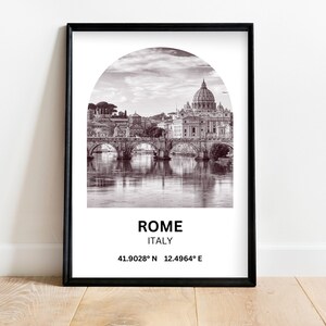 Puede incluir: Una fotografía en blanco y negro de la ciudad de Roma, Italia, con la cúpula de la Basílica de San Pedro en el fondo. La imagen está enmarcada en un marco negro e incluye el texto "ROMA, ITALIA, 41.9028° N 12.4964° E".