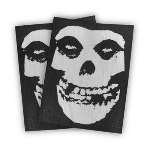 May include: Two black fabric patches with a white smiling skull design. The skull has two eye sockets, a nose, and a wide, toothy grin.