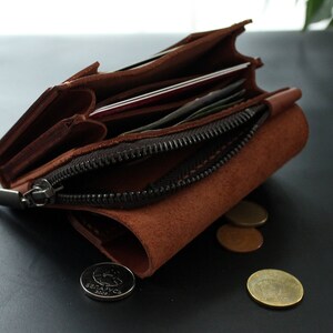 May include: A brown leather wallet with a zipper closure, open to reveal cards and cash. Several coins are scattered near the wallet. The wallet is made of a textured, suede-like material.