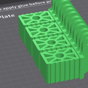 May include: A bright green 3D-printed object with a rectangular base and a curved, ridged top. The base features three stacked, square sections with circular and star-shaped cutouts. The text "Please apply glue before pr" and "A Plate" is visible.