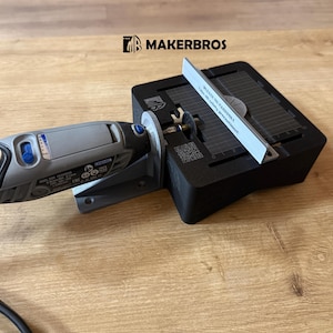 May include: A grey Dremel rotary tool mounted on a black cutting station. A white guide is in place, and the MakerBros logo is visible. The setup is on a wooden surface, suitable for precision cutting.