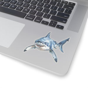 May include: A watercolor illustration of a great white shark with a white background. The shark is swimming towards the viewer with its mouth open, showing its sharp teeth.