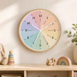 May include: A round wall clock with a light wood frame and a multicolored pastel face. The dial features black numbers 1 through 12, minute markers from 0 to 55, and text indicating time increments like O'Clock, Five Past, and Quarter To.