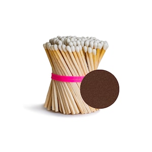 May include: A bundle of wooden matches with white tips, held together with a pink rubber band. The matches are arranged in a circle, with the tips facing outward. A brown circle is in the background.