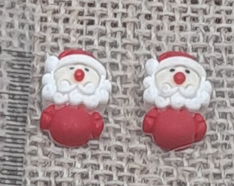May include: Two red and white Santa Claus buttons with white beards and red noses. The buttons are on a burlap background.