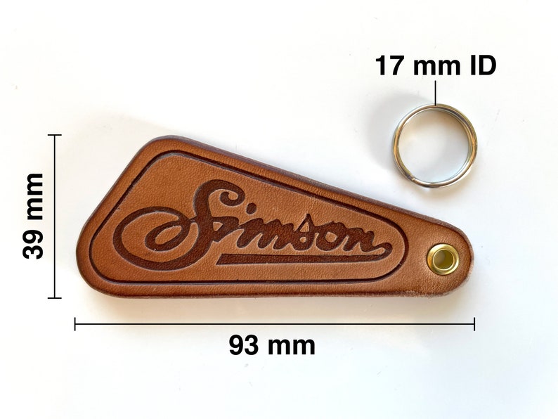 May include: Brown leather keychain with the word "Simpson" embossed in a script font. The keychain has a metal ring with a 17 mm inner diameter and measures 3.9 inches by 3.7 inches.