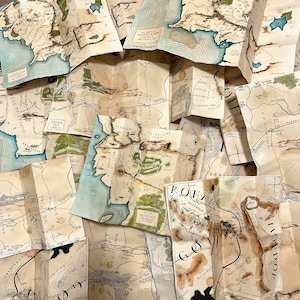 Puede incluir: Una colección de mapas plegados, con ilustraciones detalladas de paisajes, líneas costeras y texto. Los mapas son en tonos beige, marrón y azul, con etiquetas de texto. Los mapas parecen ser de un mundo de fantasía.