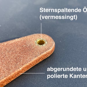 May include: Close-up of a brown leather strap with a brass star-shaped eyelet. The eyelet has rounded and polished edges. The text "Sternspaltende &Ouml;se (vermessingt)" is visible above the eyelet.