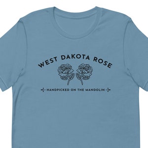 May include: A light blue t-shirt with black text that reads "West Dakota Rose" and "Handpicked on the Mandolin" with a graphic of two roses.