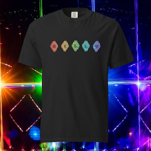 Op de afbeelding: Zwart t-shirt met een kleurrijk grafisch ontwerp. Het ontwerp toont vijf ruitvormen in regenboogkleuren, elk met een letter of symbool. De letters spellen "BILLY" met een Grieks symbool aan het einde.