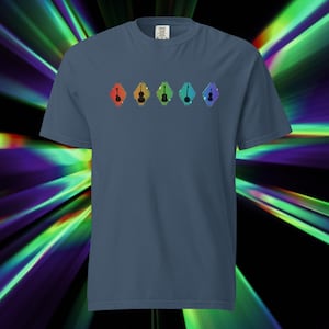 May include: A blue t-shirt featuring a row of five colorful diamond shapes, each containing a silhouette of a musical instrument. The instruments include a guitar, violin, and other stringed instruments. The shirt is made of a soft material.