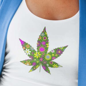 May include: White tank top with a green marijuana leaf design made of colorful flowers.