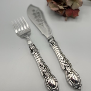 Peut inclure: Une fourchette et un couteau à beurre en argent avec des manches ornés. Les manches présentent un motif floral.