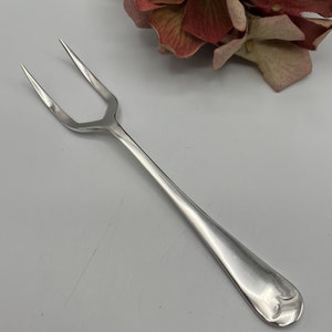 Könnte beinhalten: Eine silberne Serviergabel mit zwei Zinken und einem abgerundeten Griff.