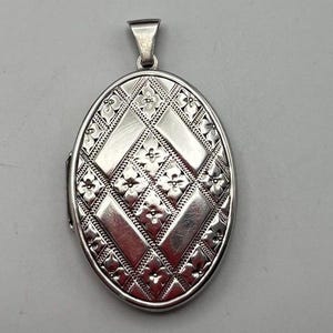 May include: Silver oval locket with a geometric design featuring a repeating pattern of diamonds and flowers.