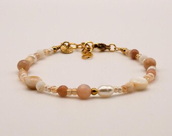 Könnte beinhalten: Ein zartes Armband mit einem Mix aus pastellrosa und weißen Perlen, darunter kleine runde Perlen, größere ovale Perlen und muschelförmige Perlen. Das Armband hat einen goldenen Verschluss.