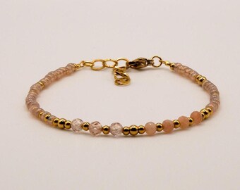 Könnte beinhalten: Ein zartes goldenes Armband mit kleinen rosa und klaren Perlen. Das Armband hat einen goldenen Verschluss.