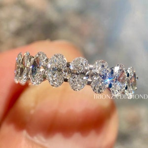 May include: A silver band ring featuring a row of oval-shaped diamonds set in a pave setting. The ring is held by a hand, and the text "TRIONZA DIAMOND" is visible in the bottom right corner of the image.
