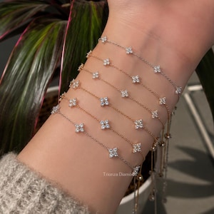May include: A set of six delicate metal chain bracelets, each featuring small, four-petaled flower-shaped charms set with clear, sparkling stones. The bracelets are worn stacked together, displaying a mix of silver and gold-toned metal finishes.