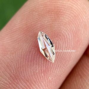 May include: A clear, faceted, kite-shaped diamond with a slight yellow hue. The diamond is set on a finger.