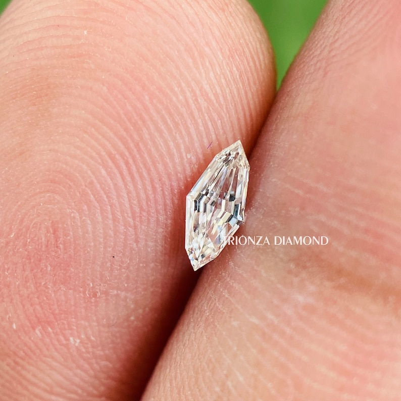 May include: A clear, faceted, octagonal-shaped diamond with a pointed top and bottom. The diamond is set on a finger.