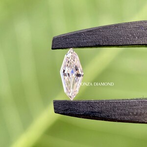 May include: A clear, faceted, elongated diamond held by black tweezers against a green background. The text "Tionza Diamond" is visible in the image.