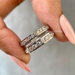 May include: A pair of silver eternity bands with a row of small diamonds set in each band. The bands are stacked on top of each other. The text "TRIONZA DIAMOND" is visible on the band.