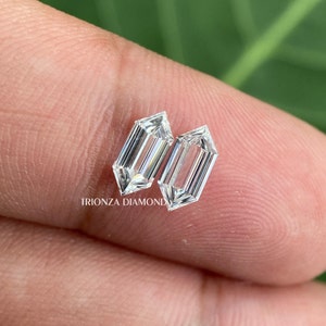 May include: Two clear, rectangular-shaped, faceted diamonds with pointed ends. The diamonds are set on a finger.
