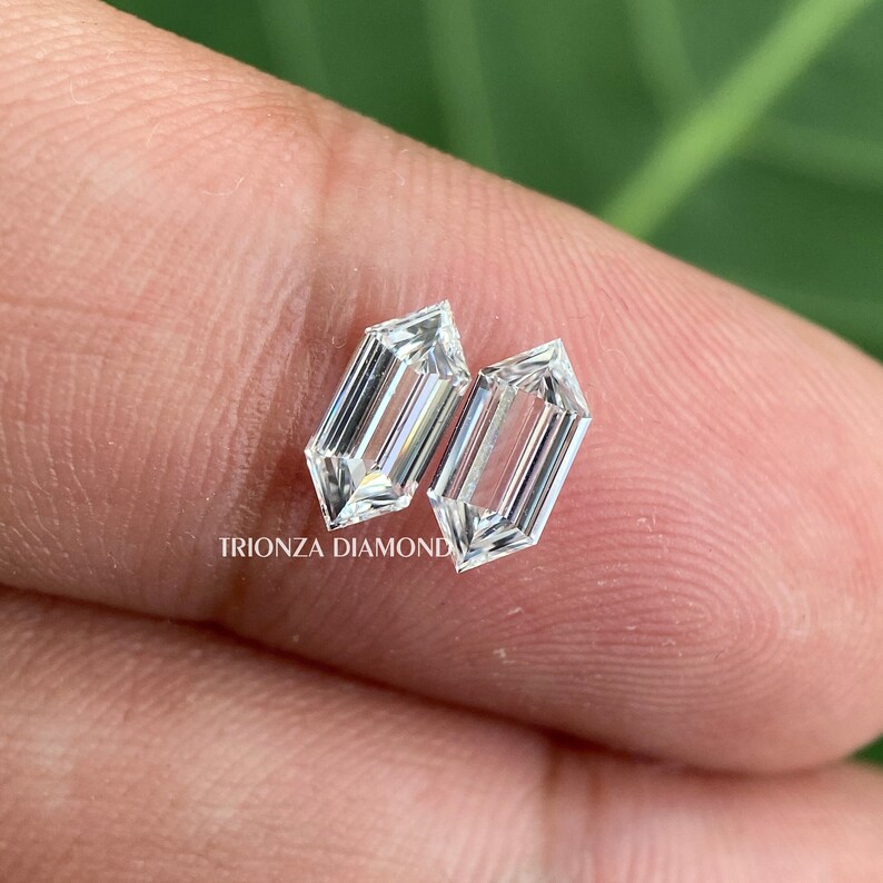 May include: Two clear, rectangular-shaped, faceted diamonds with pointed ends. The diamonds are set on a finger.
