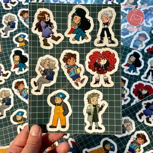 Puede incluir: Una colección de pegatinas de personajes coloridos sobre un fondo de cuadrícula verde. Las pegatinas presentan varias ilustraciones de estilo anime de personas con diferentes atuendos y poses. Algunas pegatinas tienen el texto "letter mail item!!".