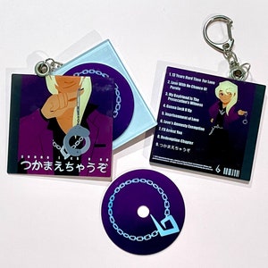 May include: A purple and blue keychain featuring a cartoon character wearing a purple jacket and handcuffs. The keychain includes a CD-shaped charm with a chain design and a rectangular charm with the text "つかまえちゃうぞ" and the title "Gunna Lock Up".
