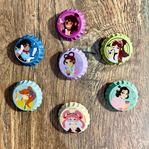 Könnte beinhalten: Satz mit sieben bunten Flaschenverschlüssen mit verschiedenen Comicfiguren. Jeder Verschluss zeigt eine andere Figur mit einem einzigartigen Design und einer einzigartigen Farbgebung. Die Verschlüsse sind perfekt, um jedem Projekt einen Hauch von Fantasie zu verleihen.