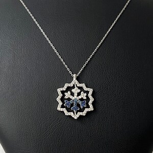 Könnte beinhalten: Eine silberne Halskette mit einem Schneeflocken-Anhänger, der mit blauen und weißen Edelsteinen besetzt ist.
