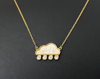 May include: A gold chain necklace with a white cloud pendant and clear crystal accents. The cloud pendant has a textured surface.