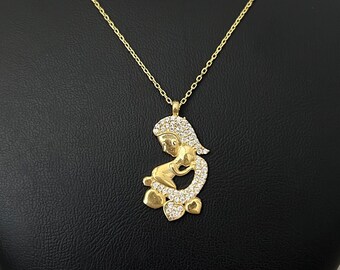 May include: A gold necklace with a pendant featuring a mother and child figure. The pendant is adorned with small, clear stones.