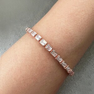 May include: A rose gold bracelet with a row of clear, rectangular-shaped stones.