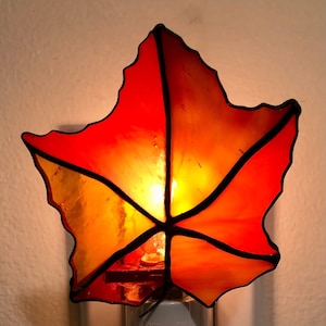 Peut inclure: Une veilleuse en forme de feuille de verre coloré avec des nuances d'orange et de jaune. La lumière est branchée sur une prise de courant et possède un interrupteur marche/arrêt.