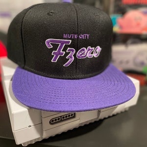 May include: A black and purple baseball cap with the text "Mute City FZero" embroidered on the front.