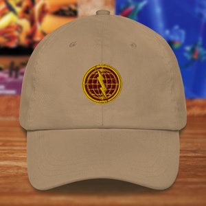 May include: A tan baseball cap with a circular embroidered patch. The patch features a gold border, a red globe, and a gold lightning bolt. The cap has a curved brim and a fabric-covered adjustable strap.