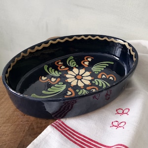 Könnte beinhalten: Eine blaue ovale Keramik-Backform mit einem weißen und grünen Blumendesign. Die Form hat einen gewellten Rand und ist glasiert.