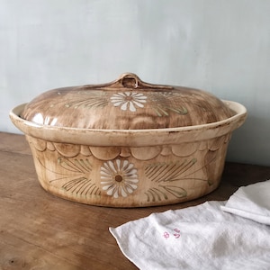 Peut inclure: Un plat de service ovale en céramique vintage avec un couvercle. Le plat est décoré d'un motif floral brun et blanc. Le plat est posé sur une surface en bois.
